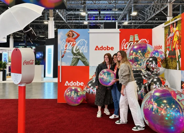 Red and white Coca-Cola Studio Booth with umbrella flash to the left of three guests at an Adobe and Coca-Cola exhibition backdrop