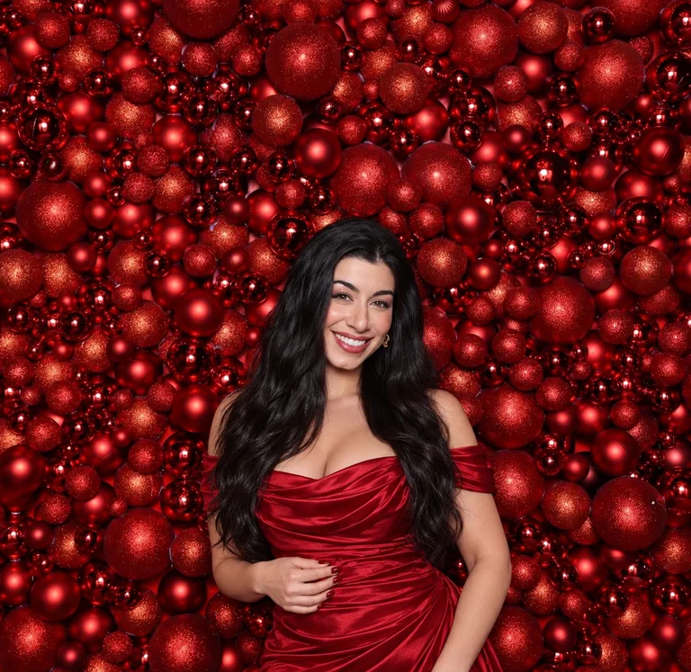 Smiling guest in a red dress posing in front of a festive red ornament backdrop