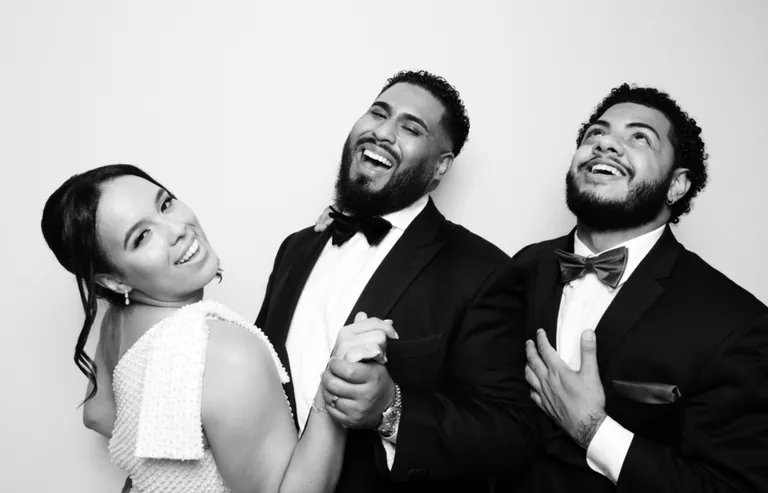 Black-and-white photo of three wedding guests in formalwear laughing together