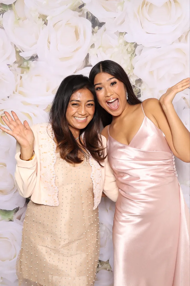 Two guests waving and laughing against a white rose backdrop