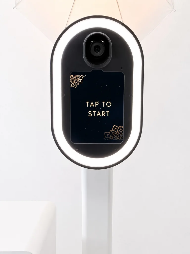 Close view of the white Studio Booth camera, illuminated ring light and touchscreen beneath an umbrella light