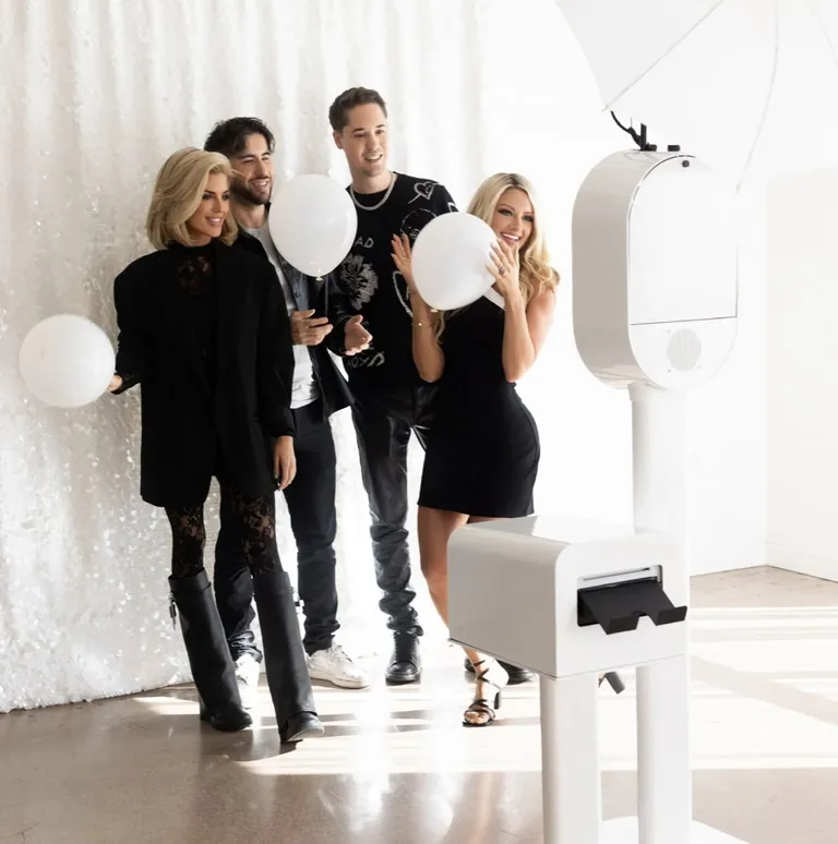 Four guests with white balloons gathered beside the white Studio Booth and printer