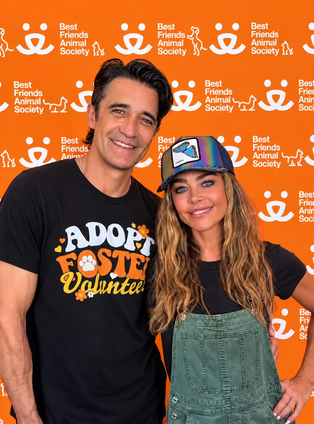 Two guests smiling in front of an orange Best Friends Animal Society event backdrop