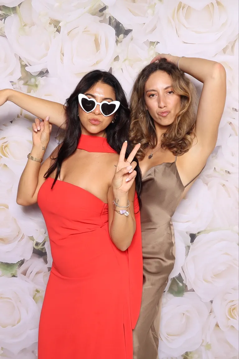 Two guests striking a playful pose against a white rose backdrop