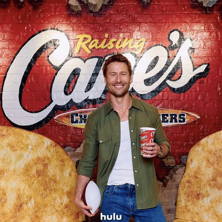 Guest smiling with a drink before a Raising Cane’s wall graphic