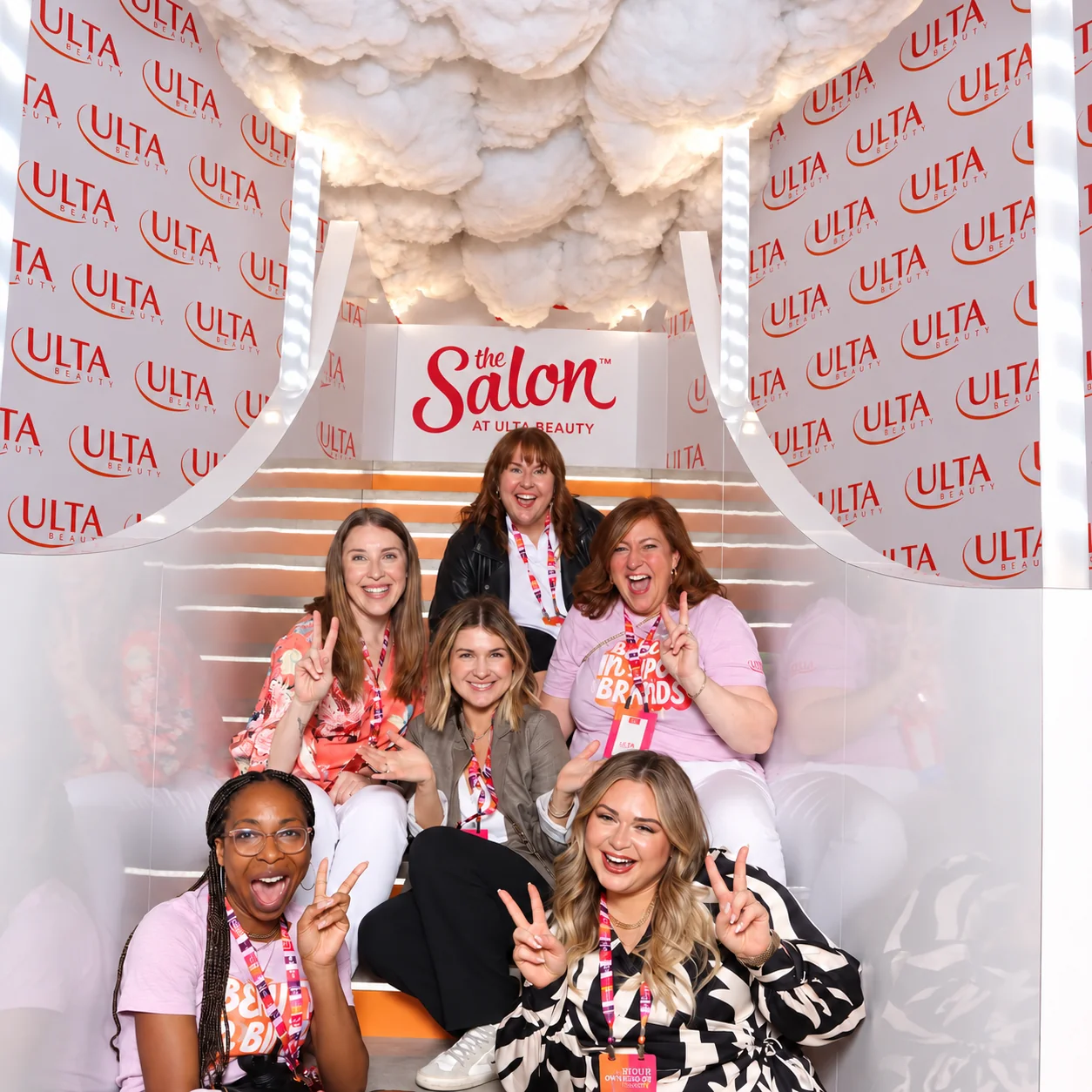 Six guests with lanyards posing on lit steps in front of The Salon at Ulta Beauty sign, between two tall ULTA-branded walls